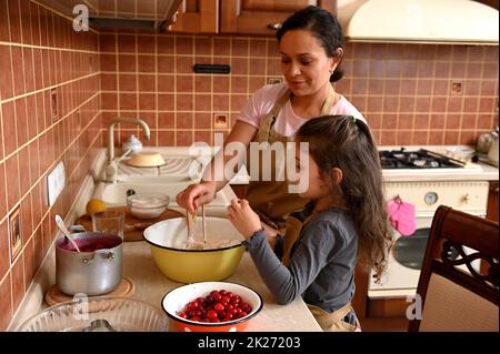 Felice famiglia multietnica, una madre amorevole e figlia che si cuocono insieme, impastando nella cucina di casa Foto Stock