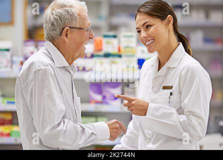 Trattando i suoi clienti con cura. Shot di un giovane farmacista che aiuta un cliente anziano. Foto Stock