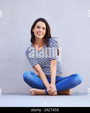 Contento di essere io. Scatto a tutta lunghezza di una bella giovane donna seduta a gambe incrociate sul pavimento. Foto Stock