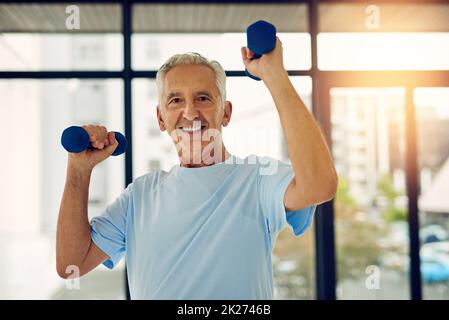 Rimanere attivi significa invecchiare bene. Ritratto di un adulto in forma sorridente mentre solleva pesi al centro fitness. Foto Stock