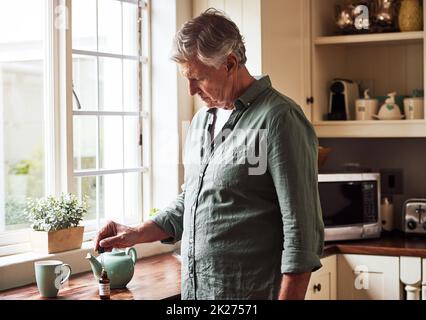 Un po' di goccia. Scatto corto di un uomo anziano rilassato che prepara una tazza di tè con olio CBD all'interno di esso a casa durante il giorno. Foto Stock