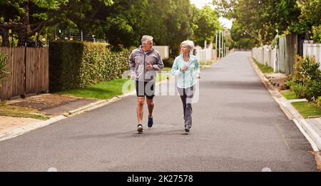 Prova a tenere il passo. Scatto di una coppia anziana allegra che ha uno scatto insieme fuori in un sobborgo. Foto Stock