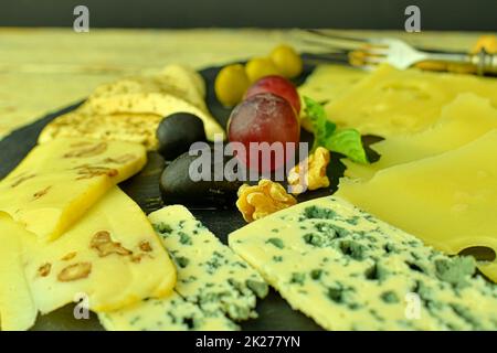 Formaggio plat. Emmental, formaggio Camembert, formaggio blu, bastoni di pane, noci, nocciole, uva su vassoio di ardesia Foto Stock