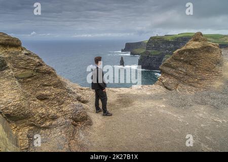 Uomo in piedi sul bordo delle iconiche scogliere di Moher, Wild Atlantic Way, Irlanda Foto Stock