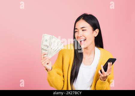 donna shopper sorridente in piedi eccitato tenere in mano il telefono cellulare intelligente online e banconote in dollari Foto Stock