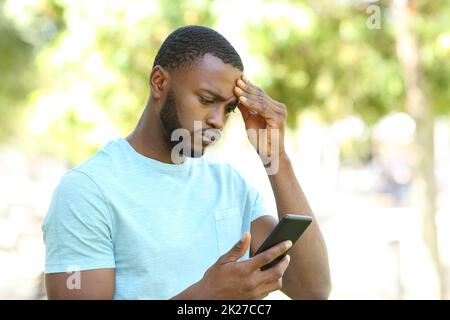 Uomo preoccupato per il controllo della pelle nera del telefono Foto Stock