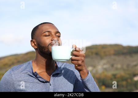 Uomo con la pelle nera che beve e che odora il caffè Foto Stock