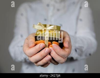 Mani che tengono la scatola del regalo d'oro isolato su sfondo grigio. Dare regalo, compleanno, Natale, giorno della madre altre feste con spazio copia Foto Stock