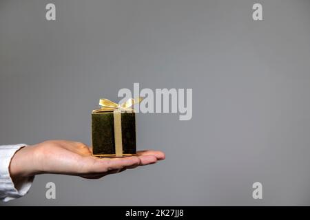 Mani che tengono la scatola del regalo d'oro isolato su sfondo grigio. Dare regalo, compleanno, Natale, giorno della madre altre feste con spazio copia Foto Stock