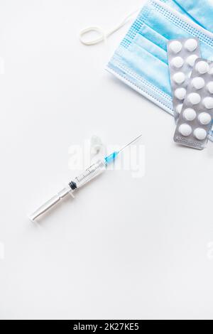 Preparazione per la vaccinazione contro il covid-19. Termometro, pillole, maschera medica su un tavolo bianco. Posto per un'iscrizione, foto verticale. Foto Stock