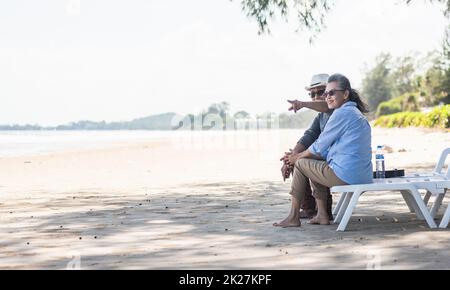 Famiglia asiatica felice, coppia anziana seduta sulle sedie con le spalle in vacanza di viaggio in spiaggia parlare insieme Foto Stock