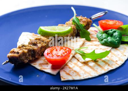 spiedino di carne alle erbe con pita pane, pomodori e lime Foto Stock