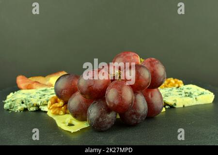 Vassoio con prosciutto di Schwarzwald, formaggi, noci, olive nere. Decorato con basilico. Cibo sul backgroud ardesia. Spazio di copia Foto Stock