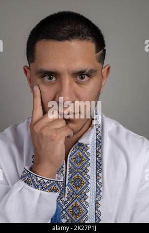dettagli del volto di un giovane uomo che guarda la telecamera con uno sguardo intimidatorio mentre pensa di avere il dito indice sul viso e una camicia Foto Stock
