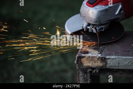 Taglierina flessibile rotante tagliando chiodo arrugginito su telaio di legno vecchio, scintille volare in aria, primo piano dettaglio Foto Stock