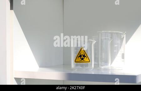 Becher con simbolo di rischio biologico su uno scaffale bianco in laboratorio. Foto Stock