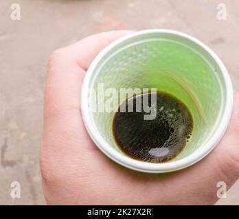 Tazza di plastica verde con caffè nero in mano di un uomo all'aperto. Un uomo tiene in mano un bicchiere di caffè. Vista dall'alto. Foto Stock