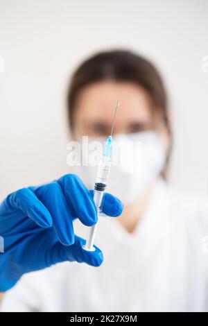 Giovane medico con una siringa in mano. Il medico al chiuso fa la vaccinazione. Una donna in un ufficio medico. Vaccinazione contro l'influenza e i virus. Foto Stock