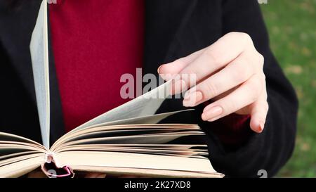 Ragazza che legge un libro nel parco. Le mani femminili sfogliano pagine di libri di carta all'aperto. Lo studente si sta preparando per l'esame. Tempo libero letterario in natura. Primo piano, spazio di copia. Foto Stock