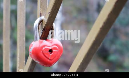 Blocco rosso Shabby a forma di cuore. Il concetto di amore di San Valentino. Un lucchetto appeso su una ringhiera metallica è un segno di amore eterno. La tradizione di agganciare un castello con una recinzione Foto Stock