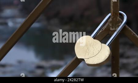 Un castello di cuori intrecciati, bloccato su una ringhiera come segno di amore eterno. Due cuori a forma di castello d'amore giallo appeso alla ringhiera del ponte Foto Stock