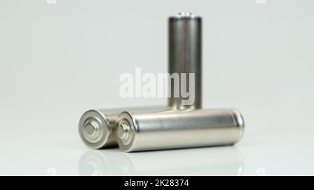 Batterie alcaline AA ricaricabili su sfondo bianco lucido con riflesso. Chiudere tre batterie scariche con spazio per la copia. Foto Stock