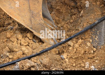 La presa di un escavatore scava terra accanto a un cavo Foto Stock