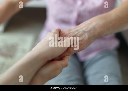 La mano della giovane ragazza tiene la mano della madre anziana. Supporto di vecchia generazione. Foto Stock