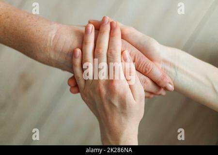 La mano della giovane ragazza tiene la mano della madre anziana. Supporto di vecchia generazione. Foto Stock