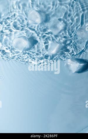 Cubetti di ghiaccio con gocce d'acqua sparse su sfondo blu, vista dall'alto. Foto Stock