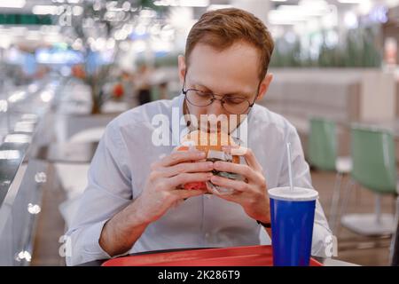 Un impiegato che mangia hamburger fast food e bibita di soda presso un'area ristoro nel centro commerciale a pranzo Foto Stock