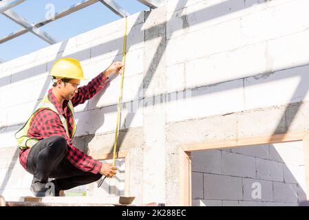 Addetto alle costruzioni o addetto alle costruzioni utilizzando il nastro di misurazione per il controllo dal telaio del tetto in acciaio alla portiera Foto Stock