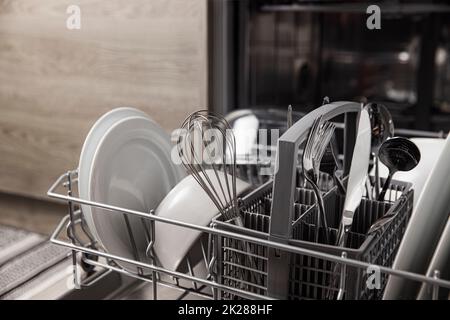 Lavastoviglie aperta con stoviglie pulite all'interno, posate, bicchieri, piatti in cucina Foto Stock