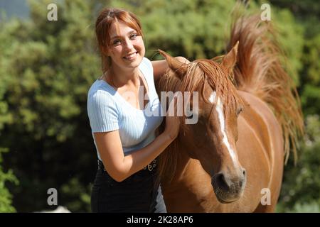 Donna felice accanto a un cavallo che ti guarda Foto Stock