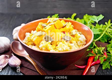 Miglio di porridge con zucca piccante in recipiente di argilla su tavola nera Foto Stock