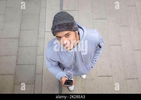 Ascoltare musica sorridente giovane latino uomo guardando in macchina fotografica runner sport allenamento dall'alto Foto Stock