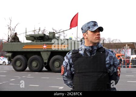 Soldato delle forze militari russe della Guardia Nazionale in giubbotto a prova di proiettile sullo sfondo di veicolo blindato su strada cittadina Foto Stock