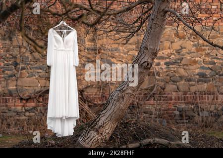 abito da sposa bianco su un albero nel cortile con una parete di mattoni sullo sfondo Foto Stock