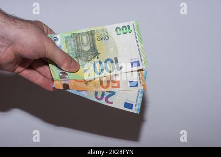 tre banconote in euro tenute in una mano al fondo con il colore grigio Foto Stock