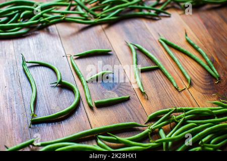 La parola fagioli fatto da baccelli su un tavolo di legno. Lavori di piantagione. Raccolta autunnale e concetto di cibo biologico sano primo piano con focus selettivo Foto Stock
