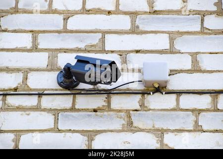 Telecamera video con illuminazione è appeso alla parete. Muro di mattoni bianchi e una videocamera con fili. Foto Stock