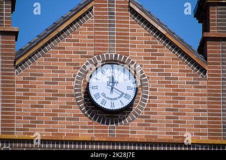 Orologio sul muro di un edificio in mattoni. Edificio in mattoni marroni con boshni e ore. Foto Stock