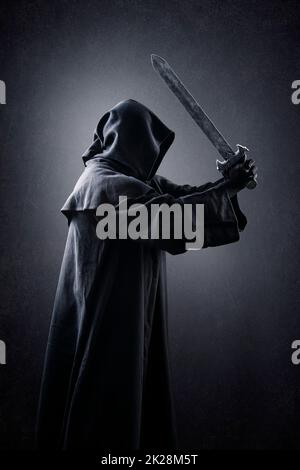 Guerriero con cappuccino e spada medievale su sfondo oscuro e confuso Foto Stock
