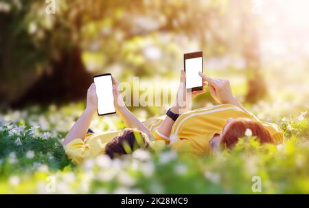 Madre e suo figlio sdraiati con i telefoni sul prato del parco Foto Stock