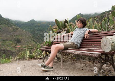 Un adolescente siede su una panchina in montagna. Tenerife. Isole Canarie. Spagna. Foto Stock