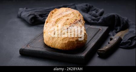 pane ovale intero cotto a forno a base di farina di grano bianco su un tavolo nero Foto Stock