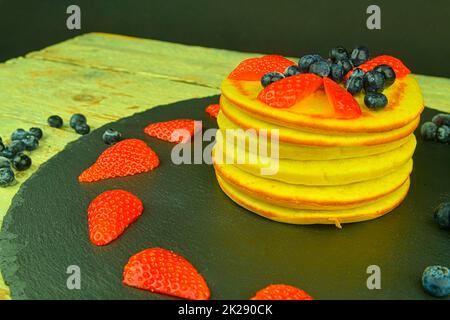 Pancake con frutti di bosco su sfondo nero. Pancake freschi. Mirtilli, fragole su pancake. Ardesia e sfondo in legno Foto Stock
