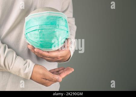 Assicurazione sanitaria in concetto COVID. Un uomo tiene una palla bianca con maschera medica verde. Lo spazio per la copia si trova sul lato destro della foto. Foto Stock