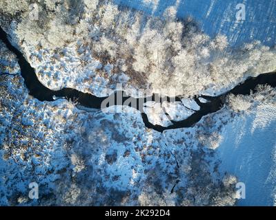 Bosco invernale con vista aerea dall'alto del gelo. Alberi sulla riva del fiume. Piccolo torrente nella foresta. Strada sterrata rurale. Campo innevato paesaggio. Clima freddo Foto Stock