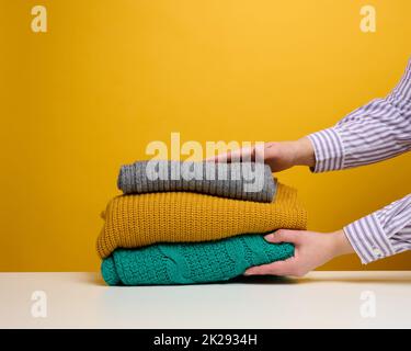 una donna tiene una pila di cose piegate lavate su uno sfondo giallo. Lavoro di routine a casa Foto Stock